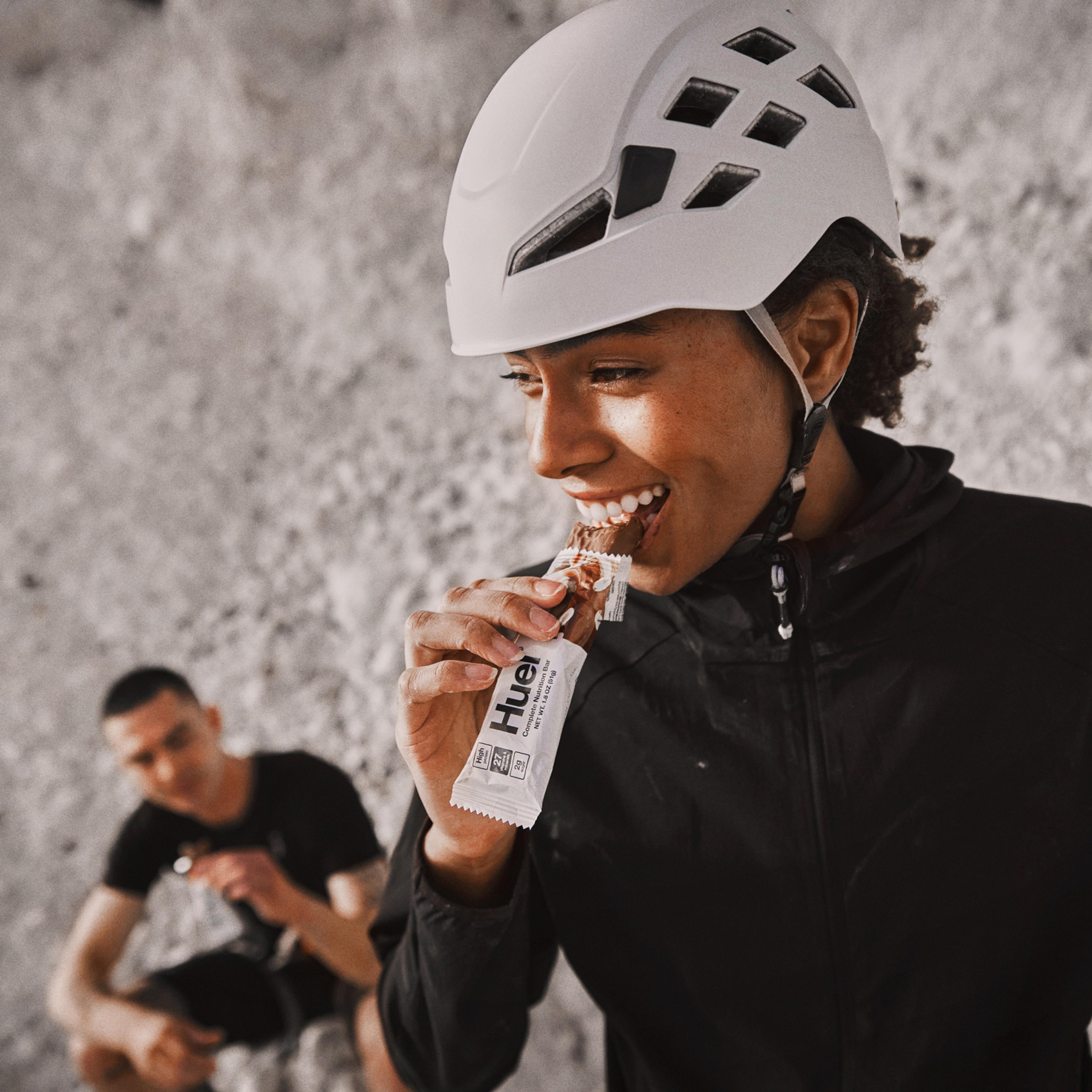 Kvinde iført en hvid cykelhjelm, der spiser en Complete Nutrition Bar. 
