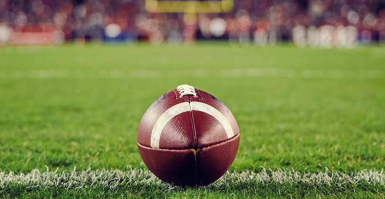 American football in the foreground on a football pitch in a stadium