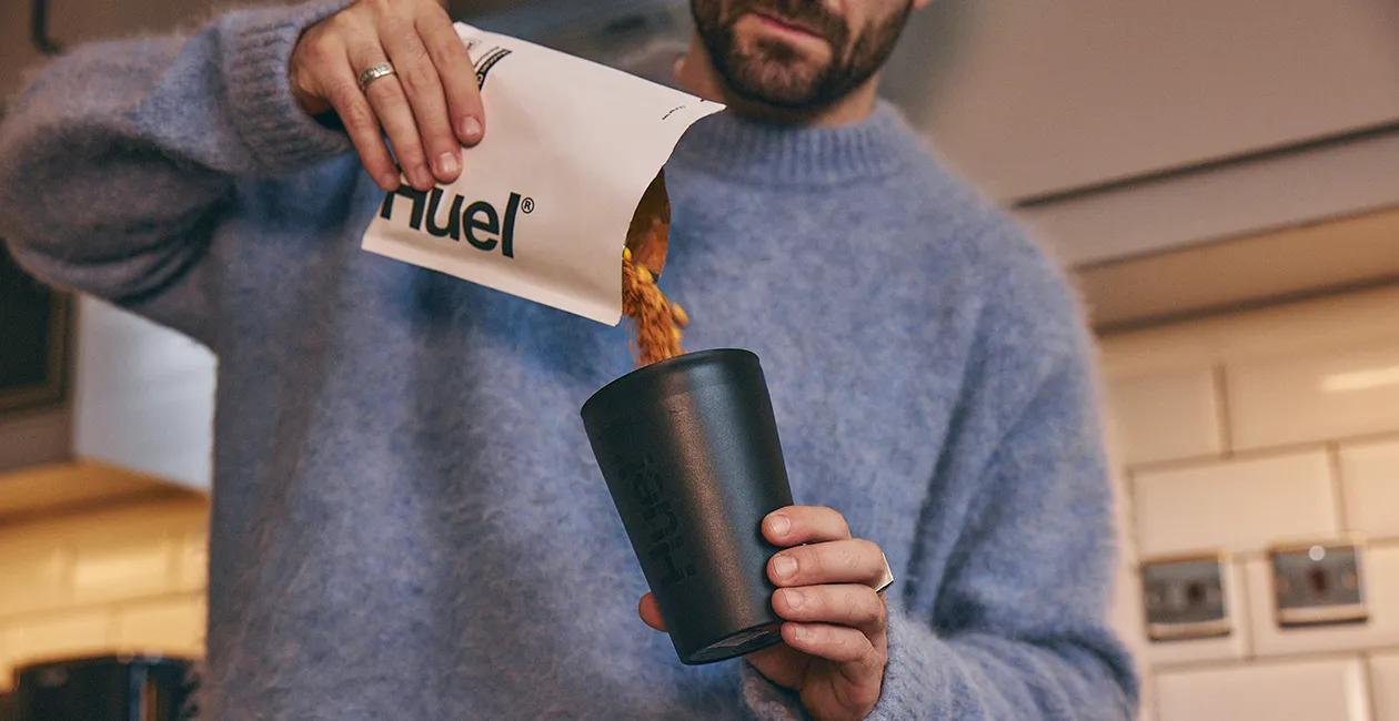 A man pouring a sachet of Huels hot and Savoury into a Huel reusable pot
