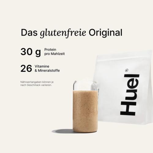 Ein Beutel Huel Pulver neben einem Glas mit einem Huel Drink vor einem neutralem Hintergrund