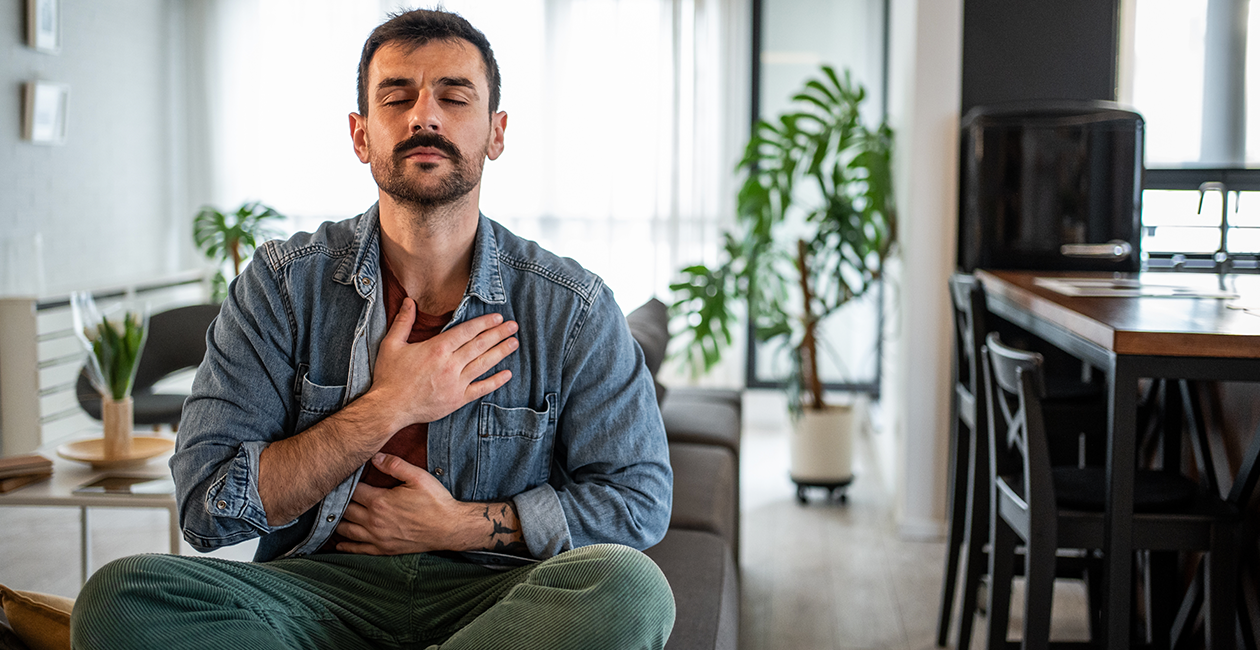 man sat cross legged with his eyes closed and hand on his chest concentrating on his breathing