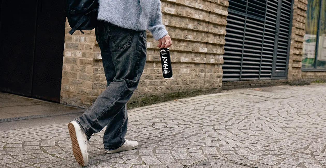 person walking along a path outside holding a Huel Black Edition Ready-to-drink