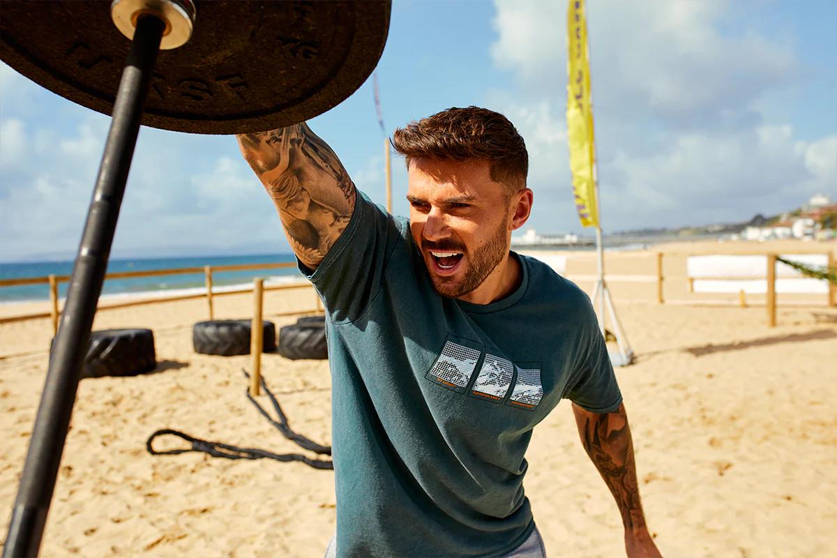 Man on a beach lifting barbell and weight from one end