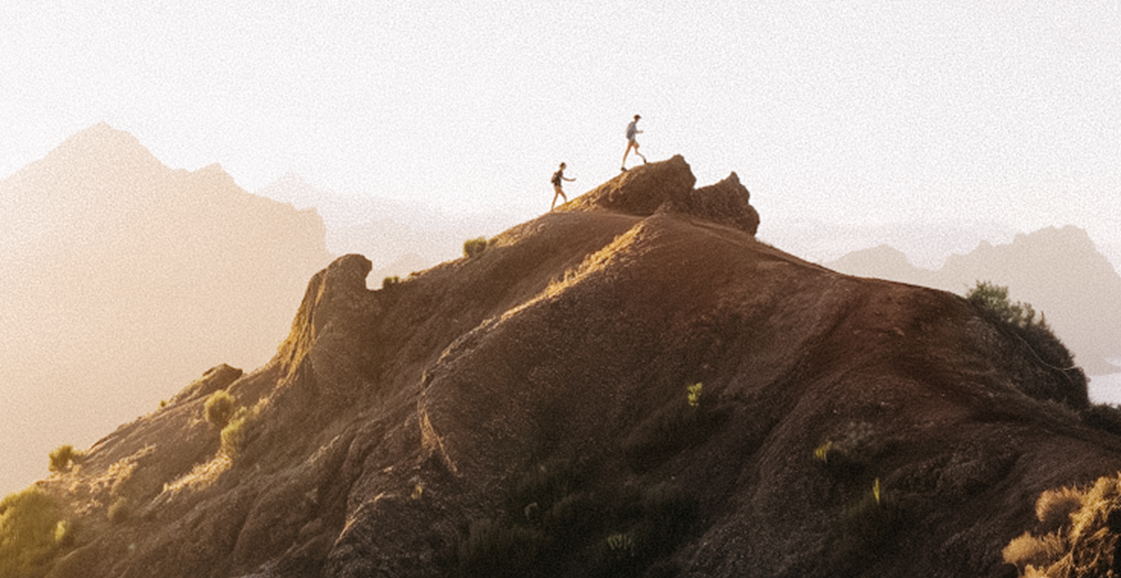 two people at the summit of a mountain with other mountains in the background