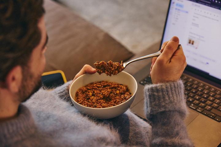A man eating Hot & Savoury out a bowl with a fork looking at his laptop