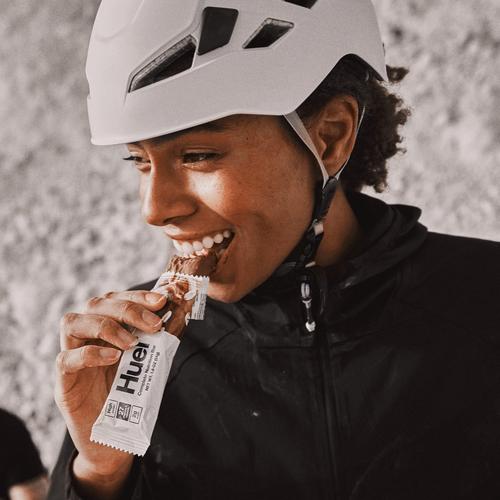 A woman wearing a white bike helmet eating a Huel Complete Nutrition protein bar during a bike ride