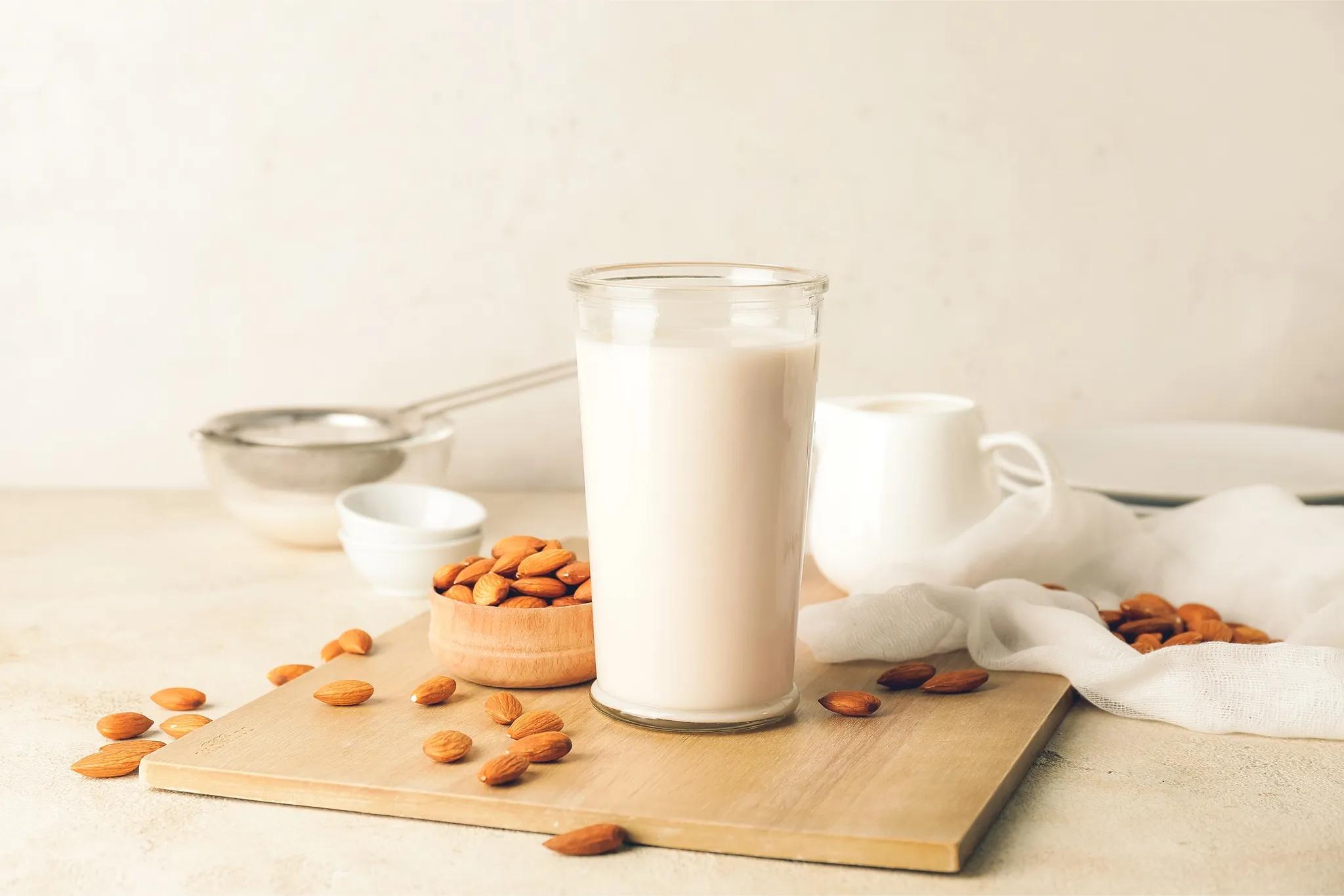 glass of almond milk on a wooden board surrounded by loose almonds