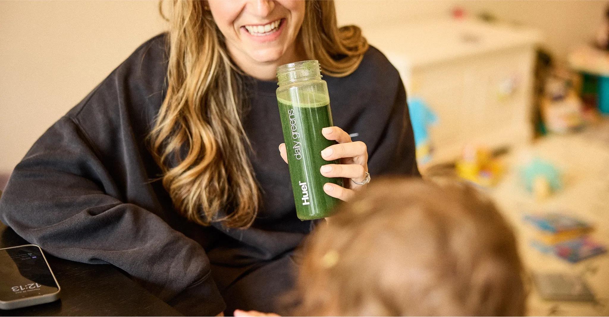 woman smiling while holding a Huel Daily Greens Powder drink