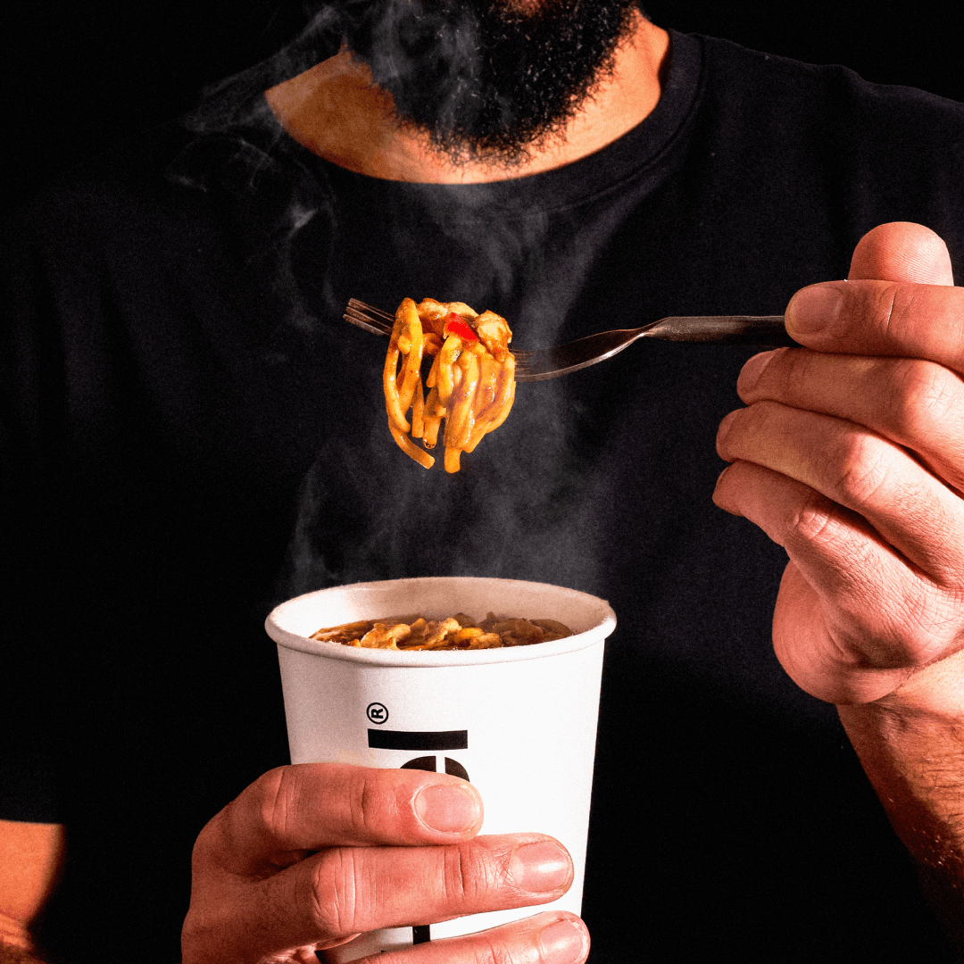 En mand iført en sort t-shirt, der spiser Huel Hot & Savory Noodles på en gaffel