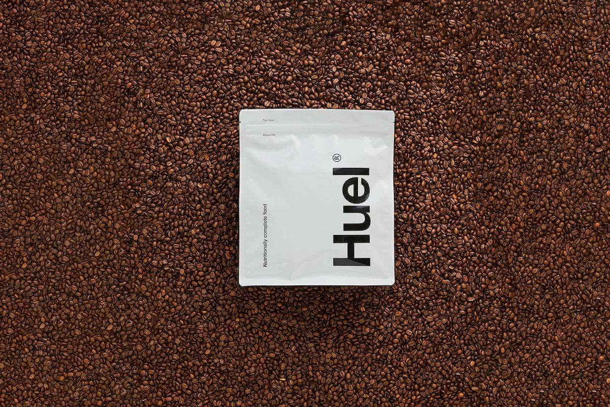 A bag of Huel Original Powder laying on a background of coffee beans