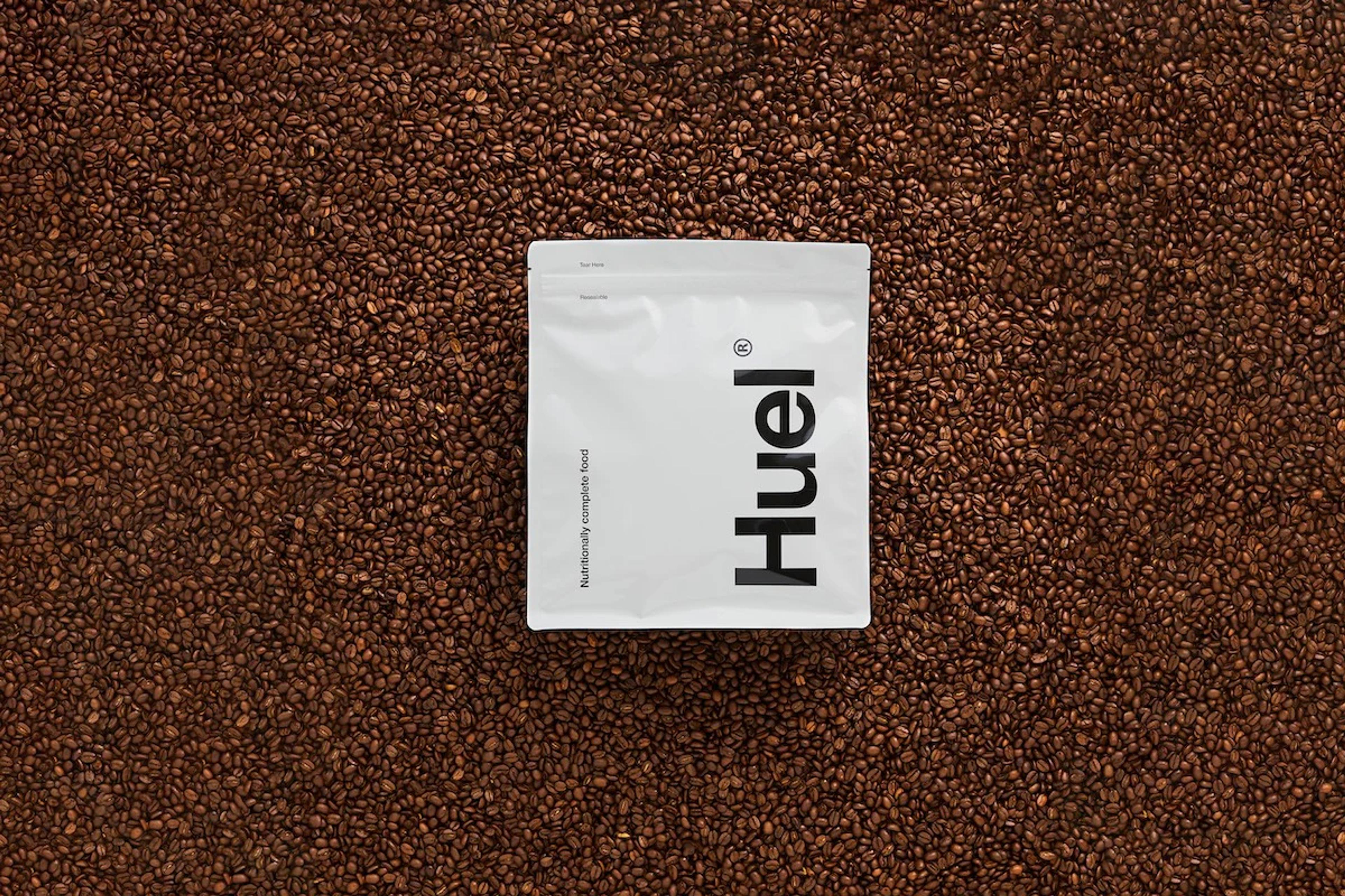 A bag of Huel Original Powder laying on a background of coffee beans