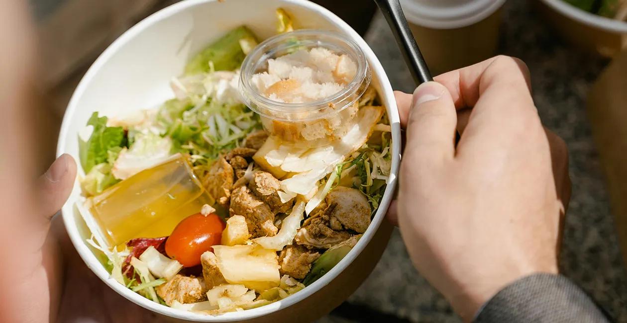 a person holding a chicken salad with croutons and dressing in a bowl
