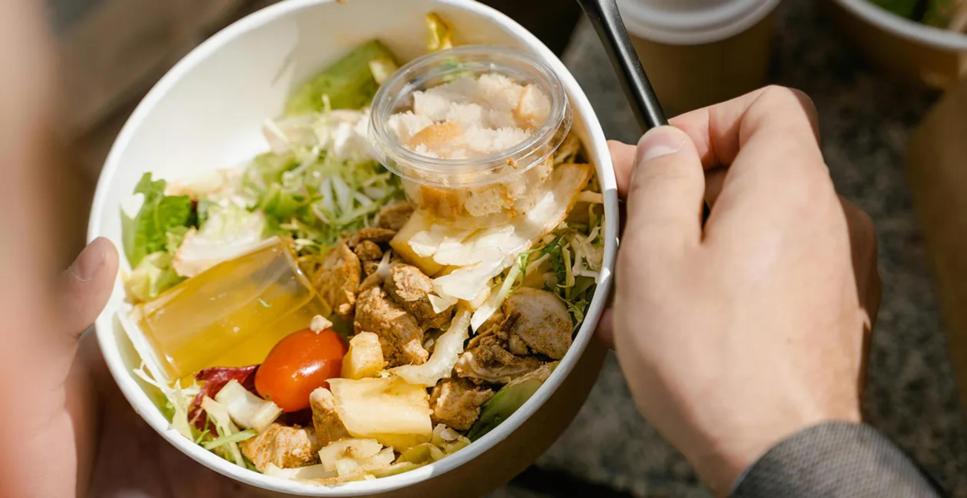 a person holding a chicken salad with croutons and dressing in a bowl