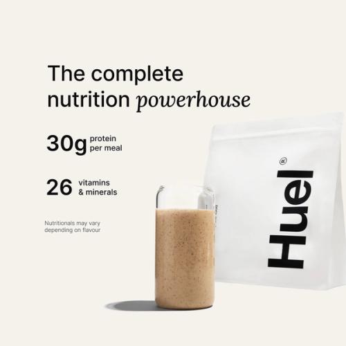 A bag of Huel powder next to a glass containing a Huel drink on a neutral background