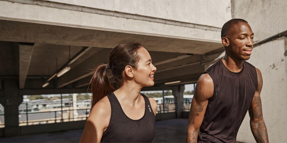 man and woman walking in the sun wearing athletic gear and holding a Huel shaker