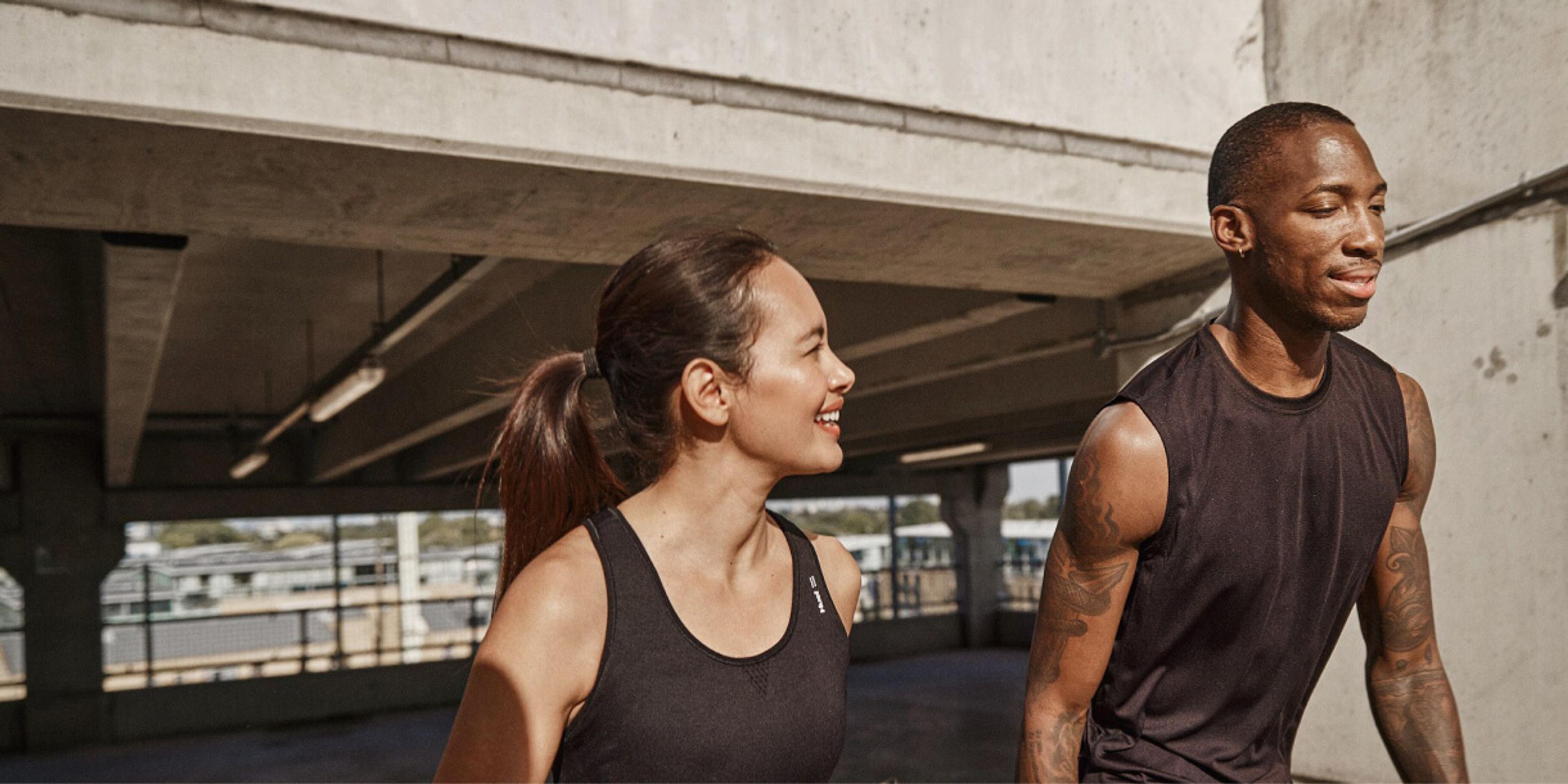 man and woman walking in the sun wearing athletic gear and holding a Huel shaker