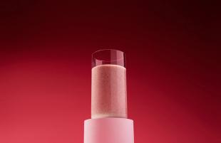 A glass with strawberry Huel Black Edition Powder on a red background