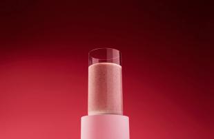 A glass with strawberry Huel Black Edition Powder on a red background