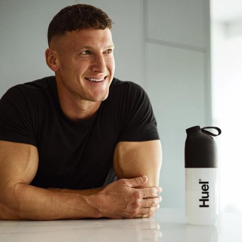 Bodybuilder matt morsia sat next to a black and white Huel shaker in a kitchen