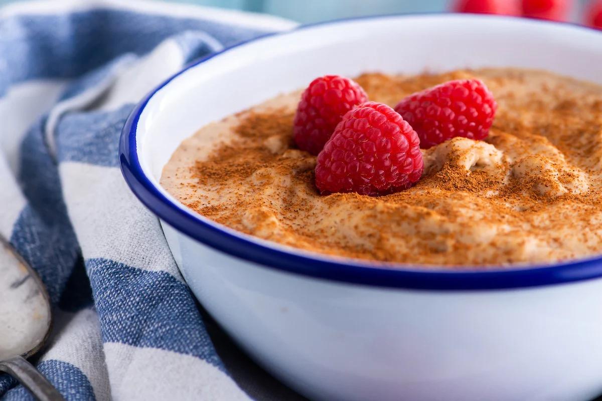 a bowl of porridge with powdered cinnamon and raspberries on top