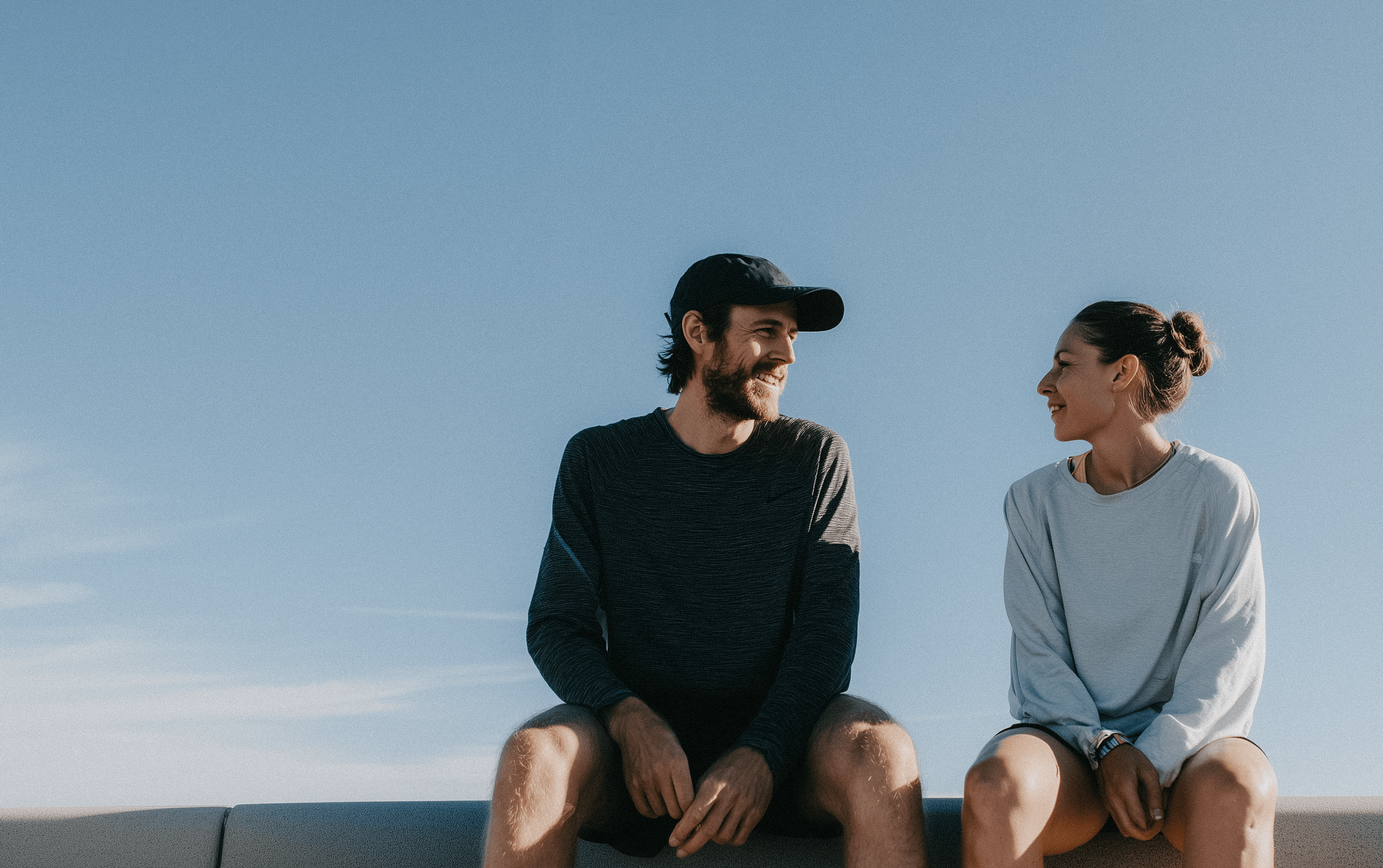 Glimlachende vrouw die een man met baard hartelijk aankijkt, wat verbondenheid en vertrouwen uitstraalt - en weergeeft hoe Huel Plus beloningen alledaagse momenten kan verbeteren.