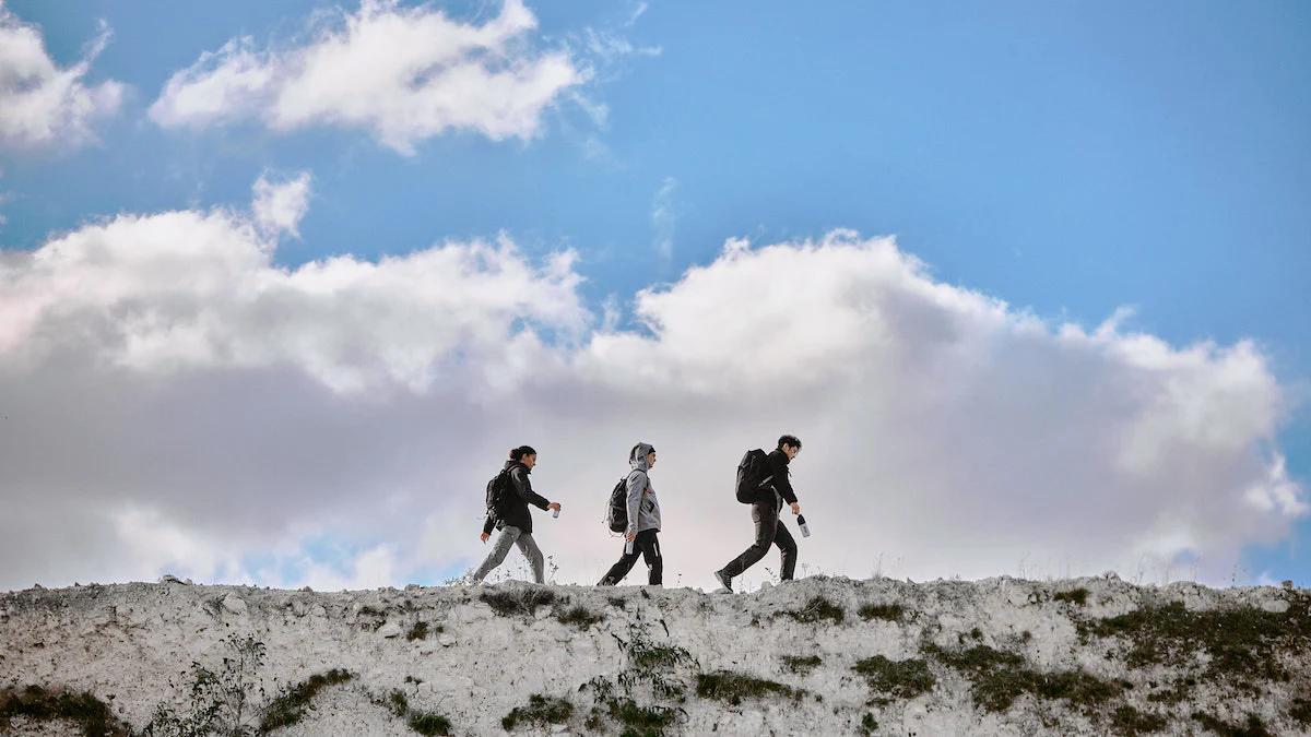 three people hiking along the top of a rock with blue skies and clouds behind them