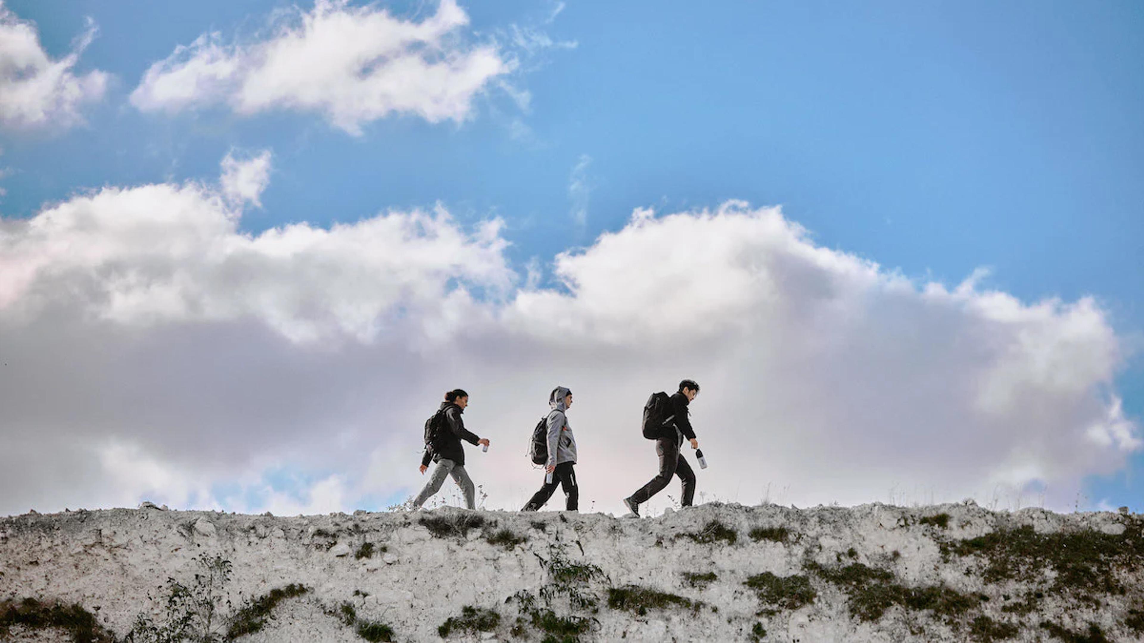 three people hiking along the top of a rock with blue skies and clouds behind them