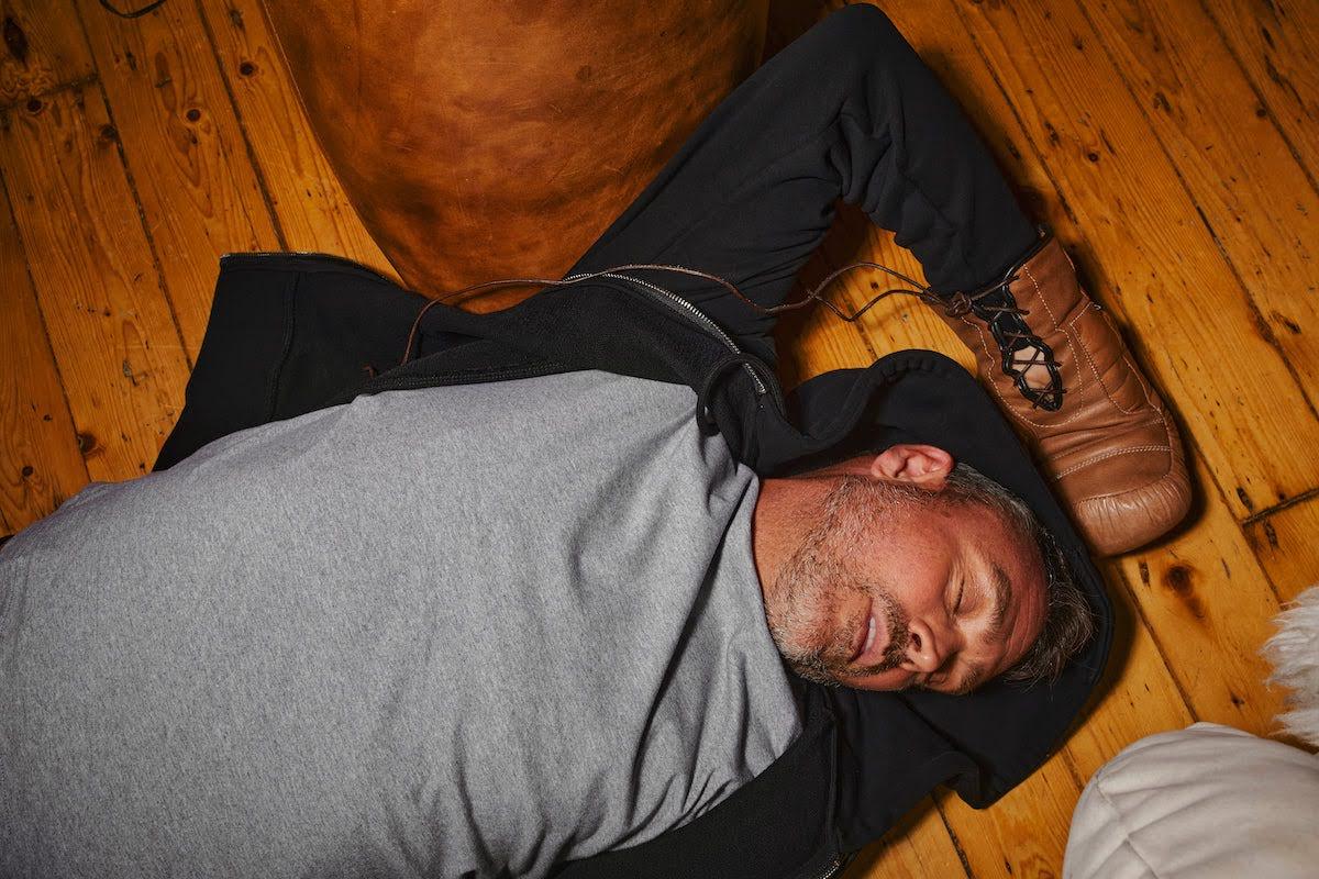 man laying on the ground with a boxing glove on and his eyes shut