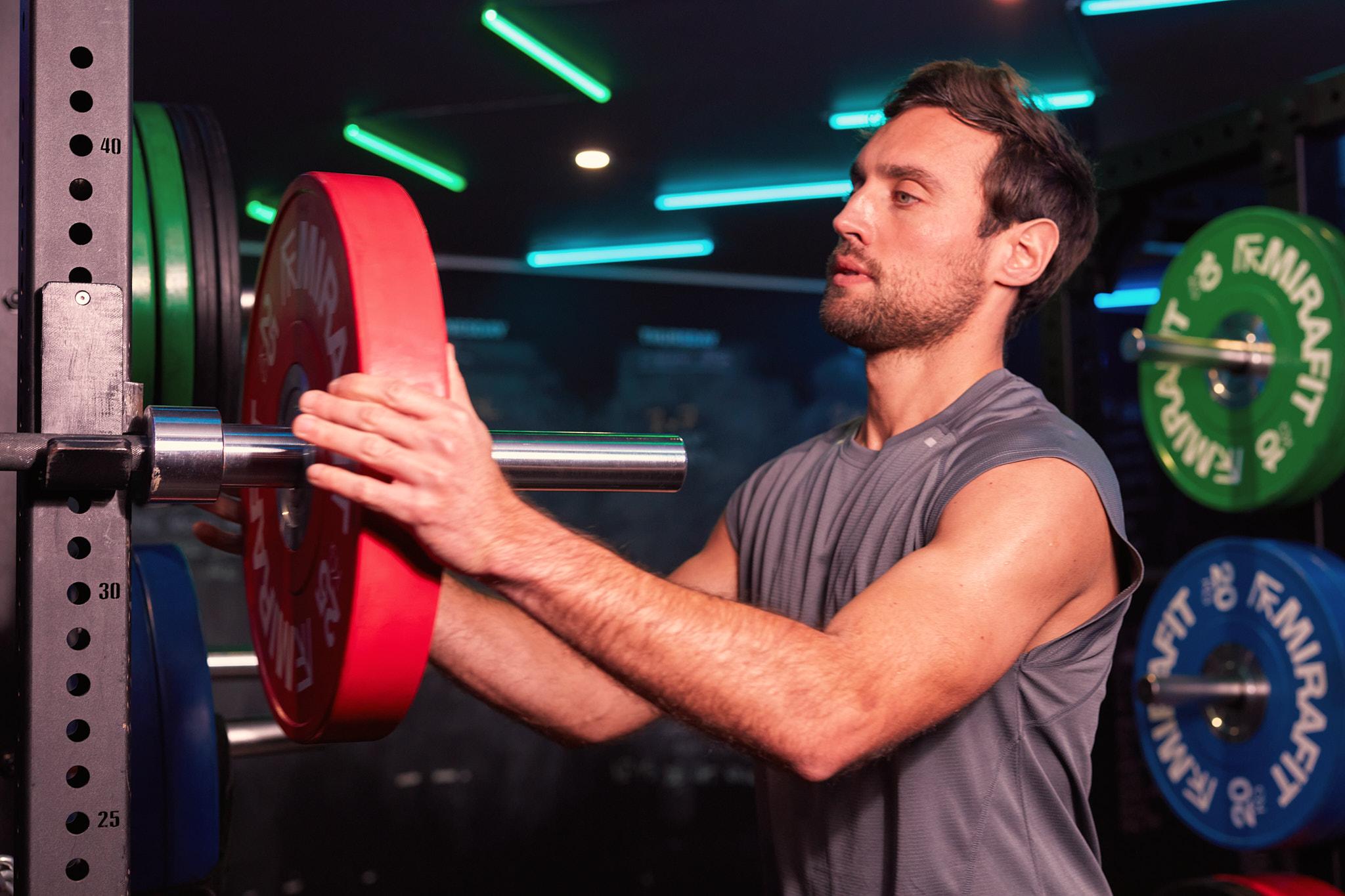 man loading weight onto a barbell on a squat rack