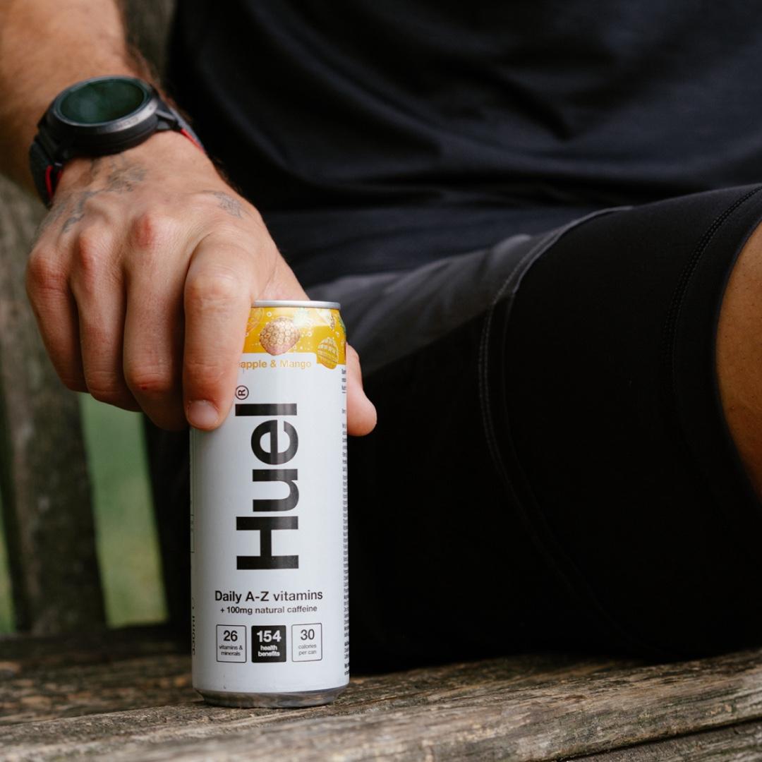 A man placing a can of Huel Daily A-Z Vitamins energy drink on a wooden park bench
