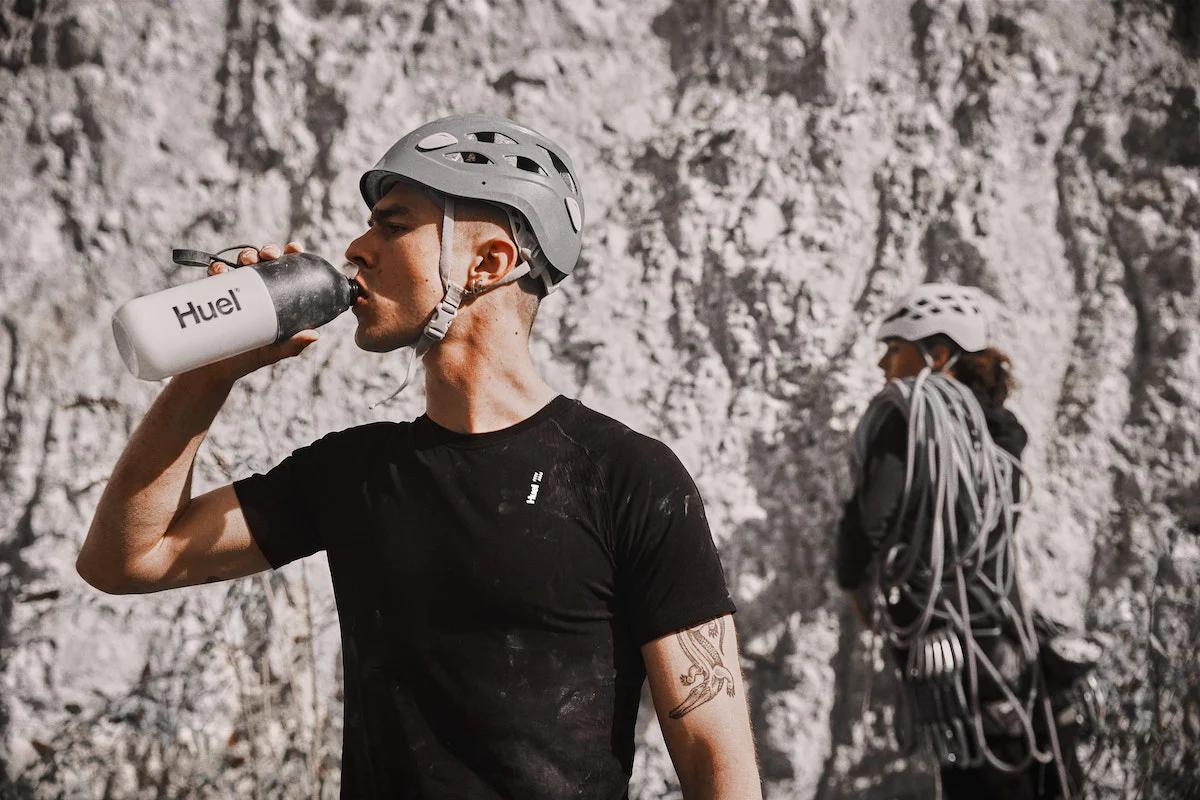 rock climber wearing a helmet and drinking from a huel shaker in front of rocks