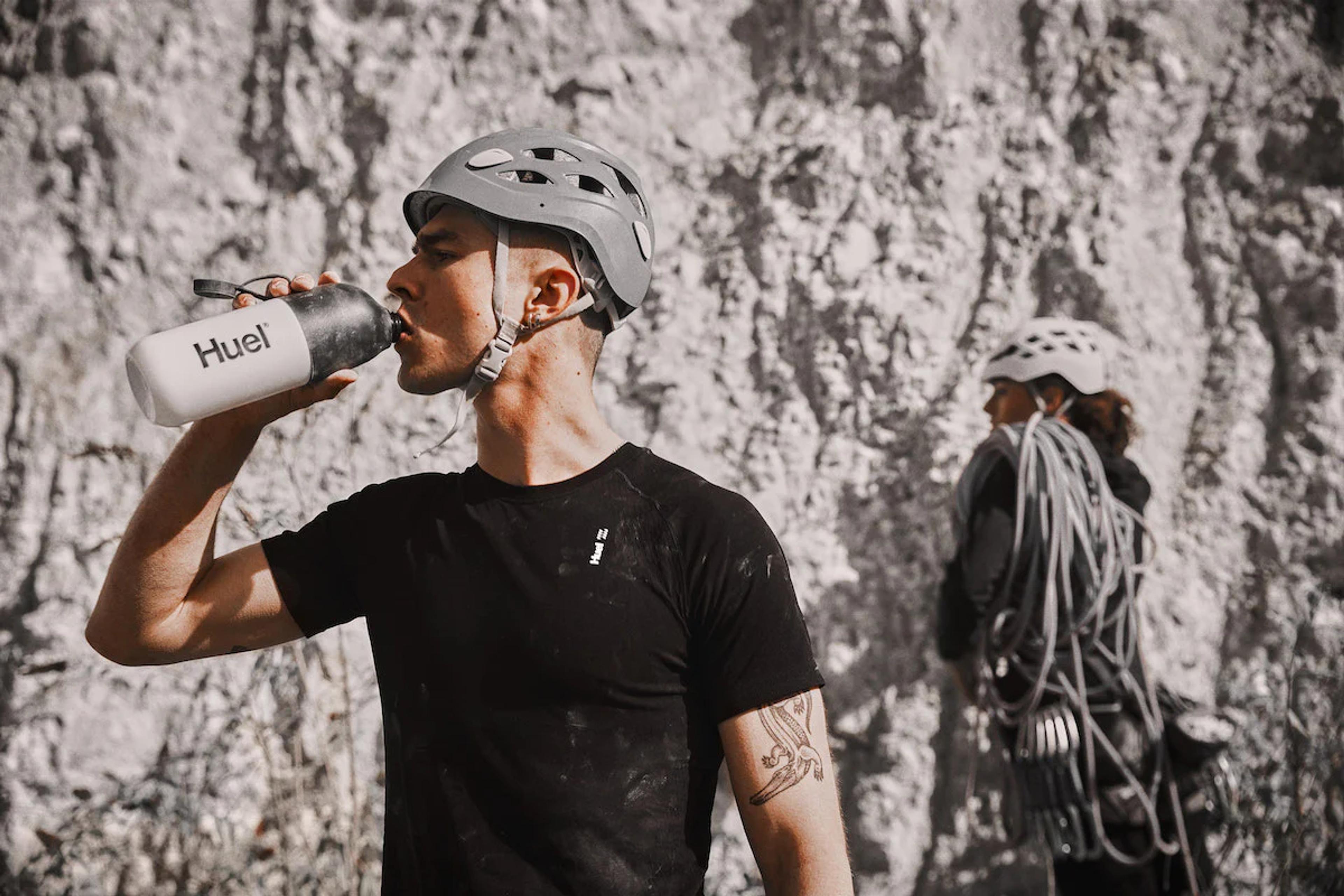 rock climber wearing a helmet and drinking from a huel shaker in front of rocks