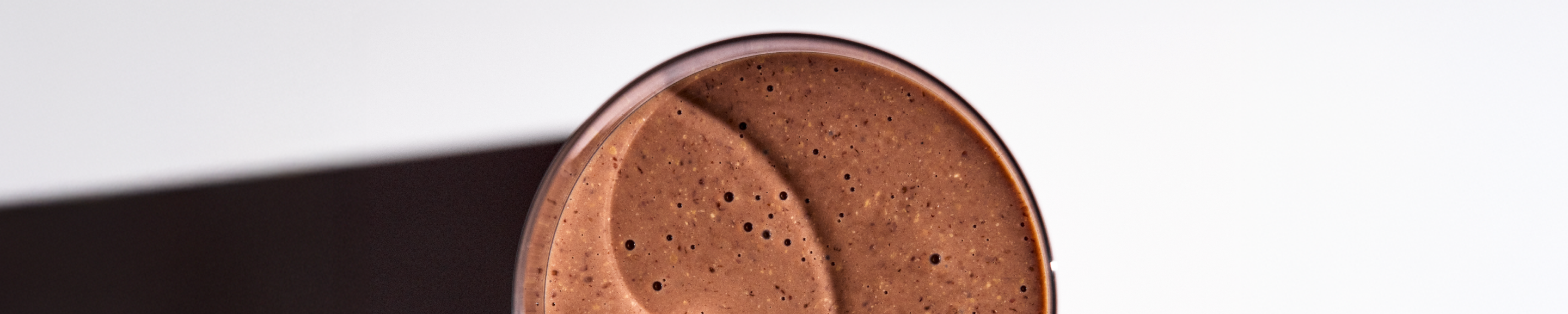 a close-up image of a glass of chocolate Huel shake set against a grey background