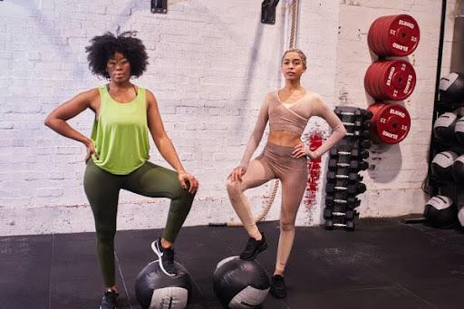 two women stood in  gym with a foot on a medicine ball