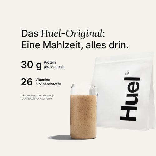 Ein Beutel Huel Pulver neben einem Glas mit einem Huel Drink vor einem neutralem Hintergrund