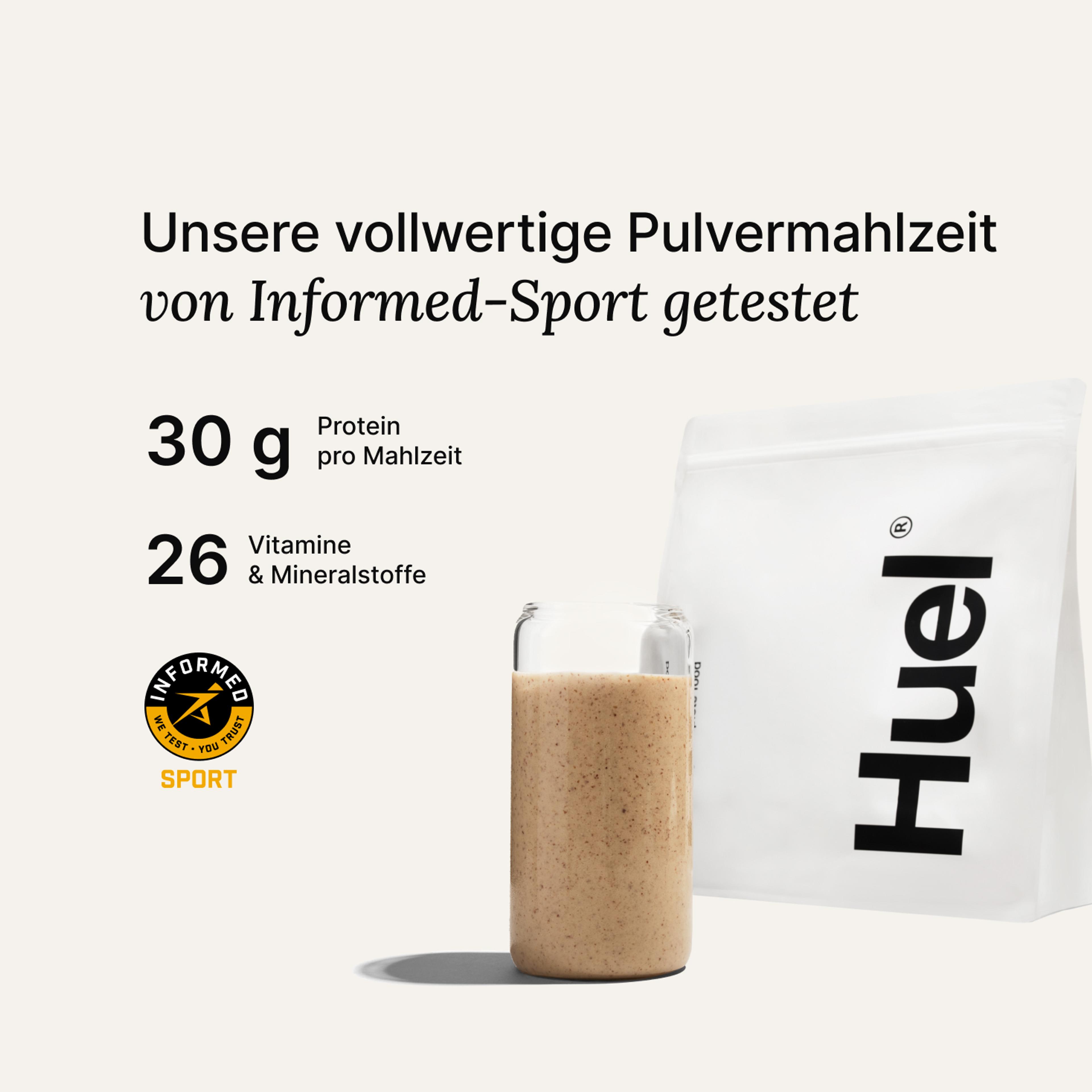 Ein Beutel Huel Pulver neben einem Glas mit einem Huel Drink vor einem neutralem Hintergrund