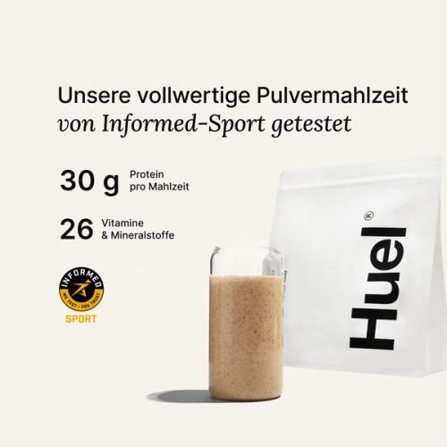 Ein Beutel Huel Pulver neben einem Glas mit einem Huel Drink vor einem neutralem Hintergrund