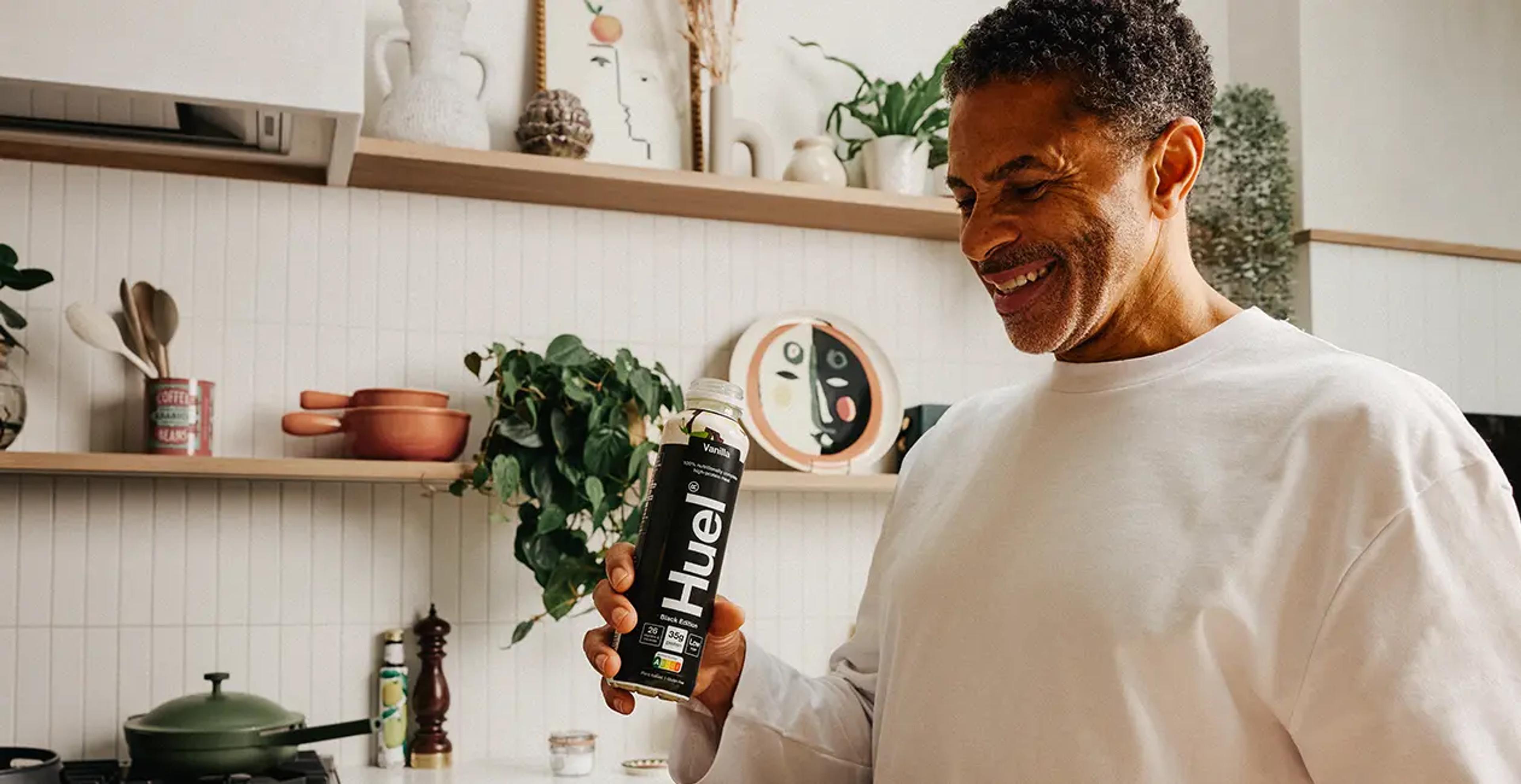 man stood in kitchen holding a Huel Black Edition Ready-to-drink meal replacement and smiling