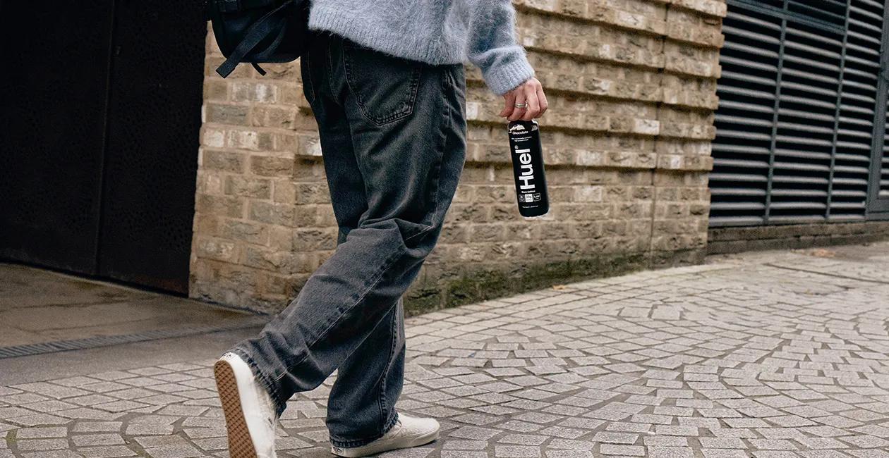 person walking along a street holding a Huel Black Edition Chocolate