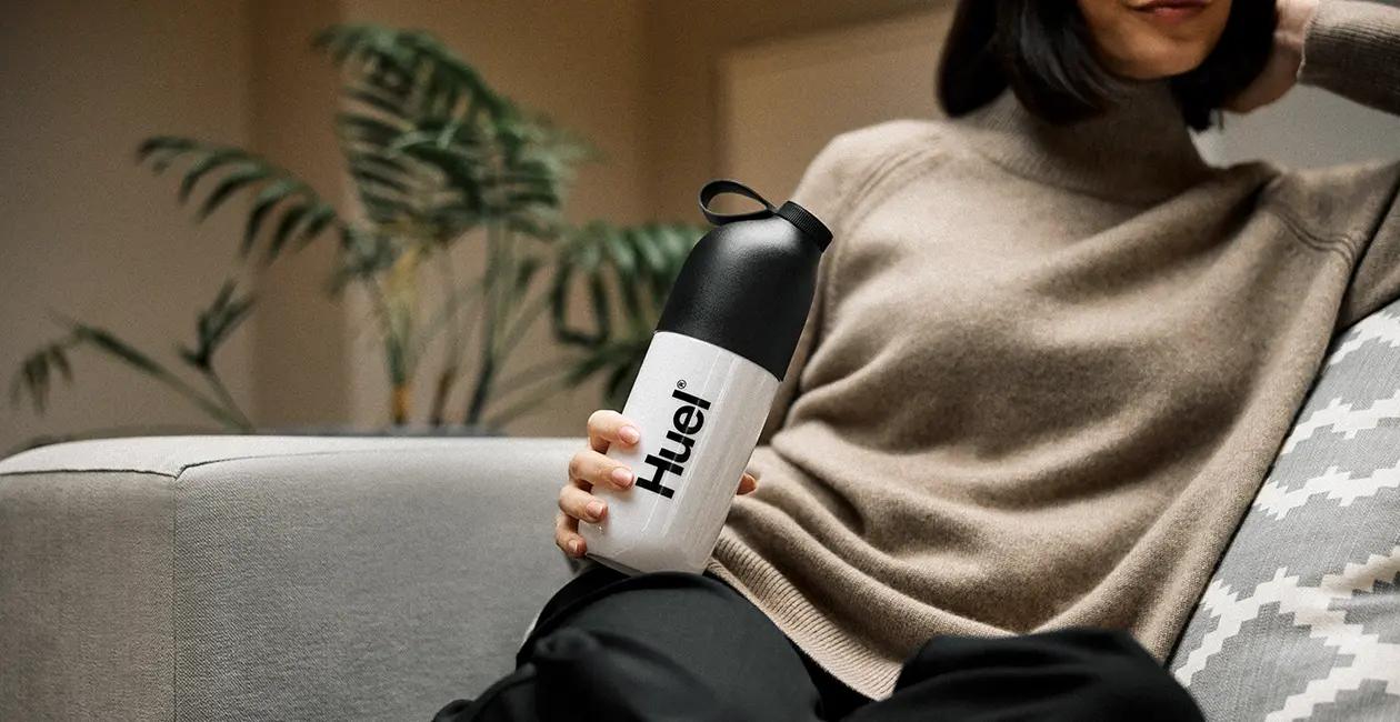 woman on a sofa holding a Huel shaker