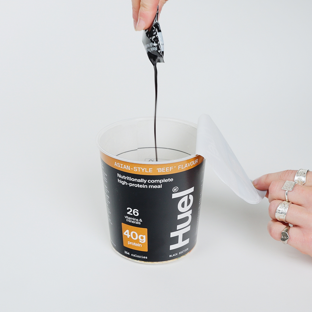 Someone pouring a sachet of sauce into the Huel Black Edition Ramen pot