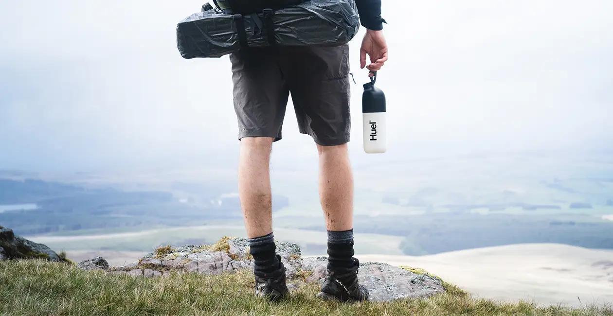man stood atop a hill overlooking the countryside holding a huel shaker