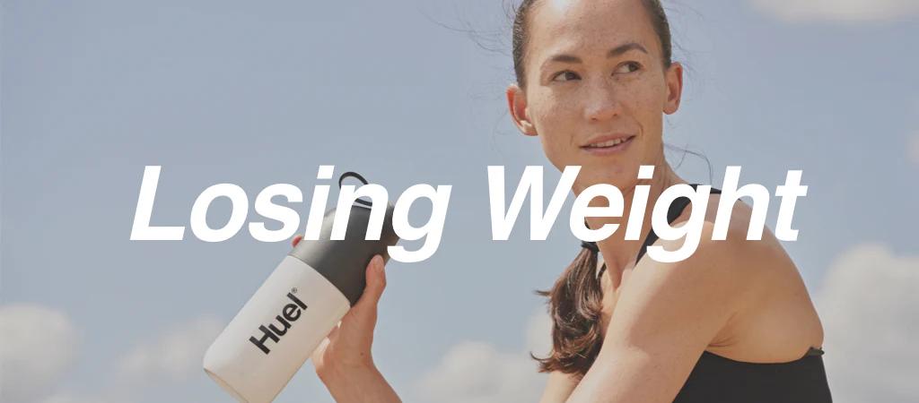 Young woman holding a Huel shaker against a blue sky with white clouds