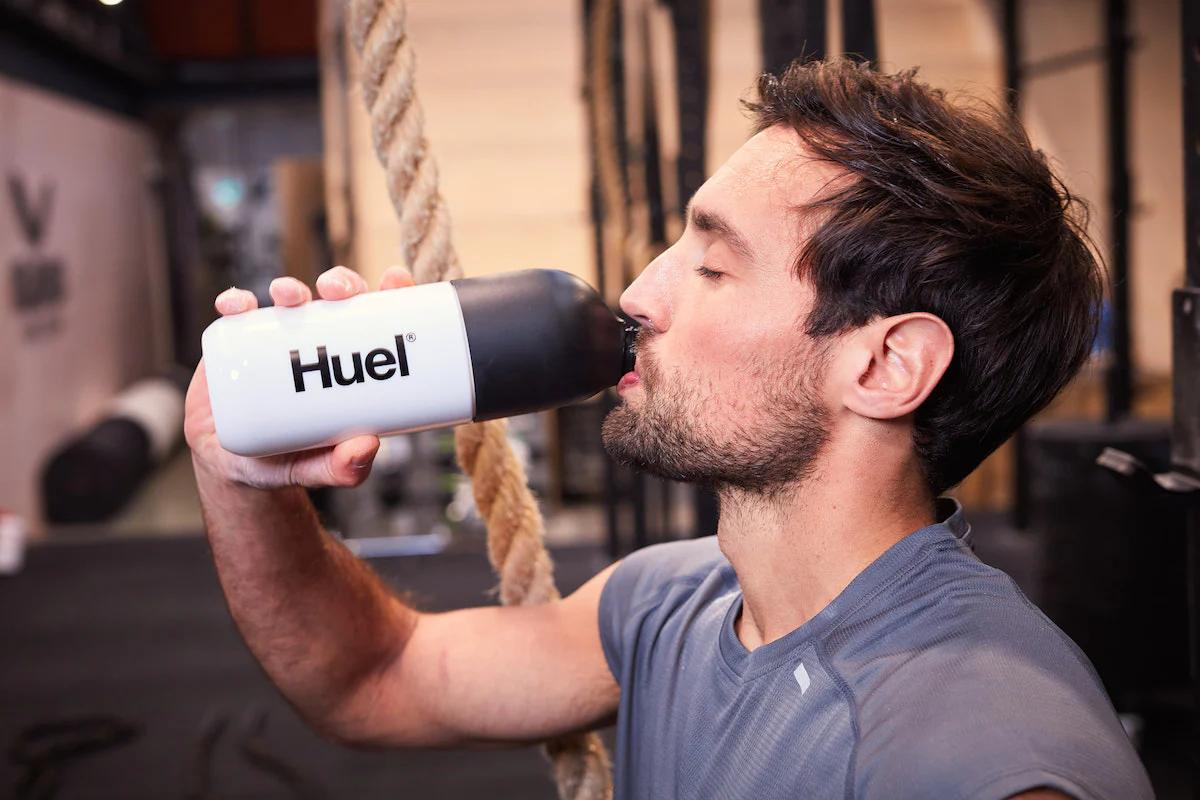 man sat in a gym drinking huel from a huel shaker