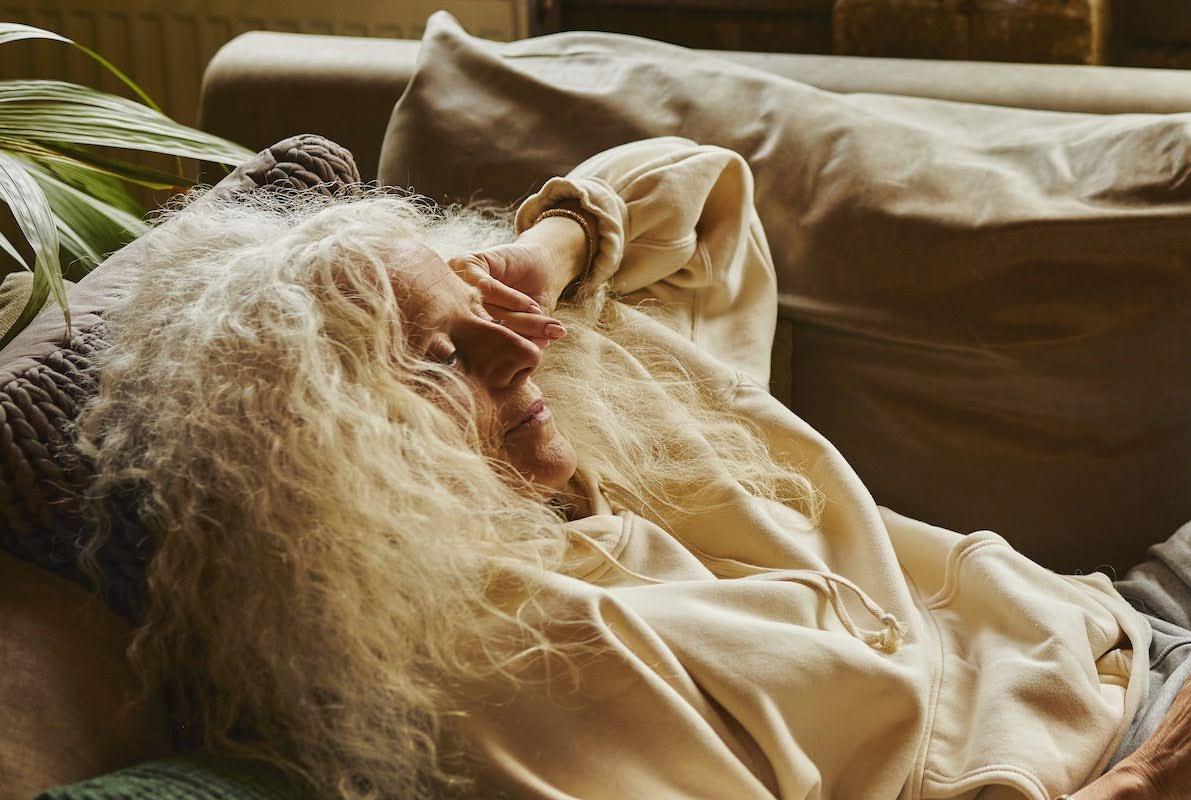 older woman laying on a sofa with her hand resting on her head