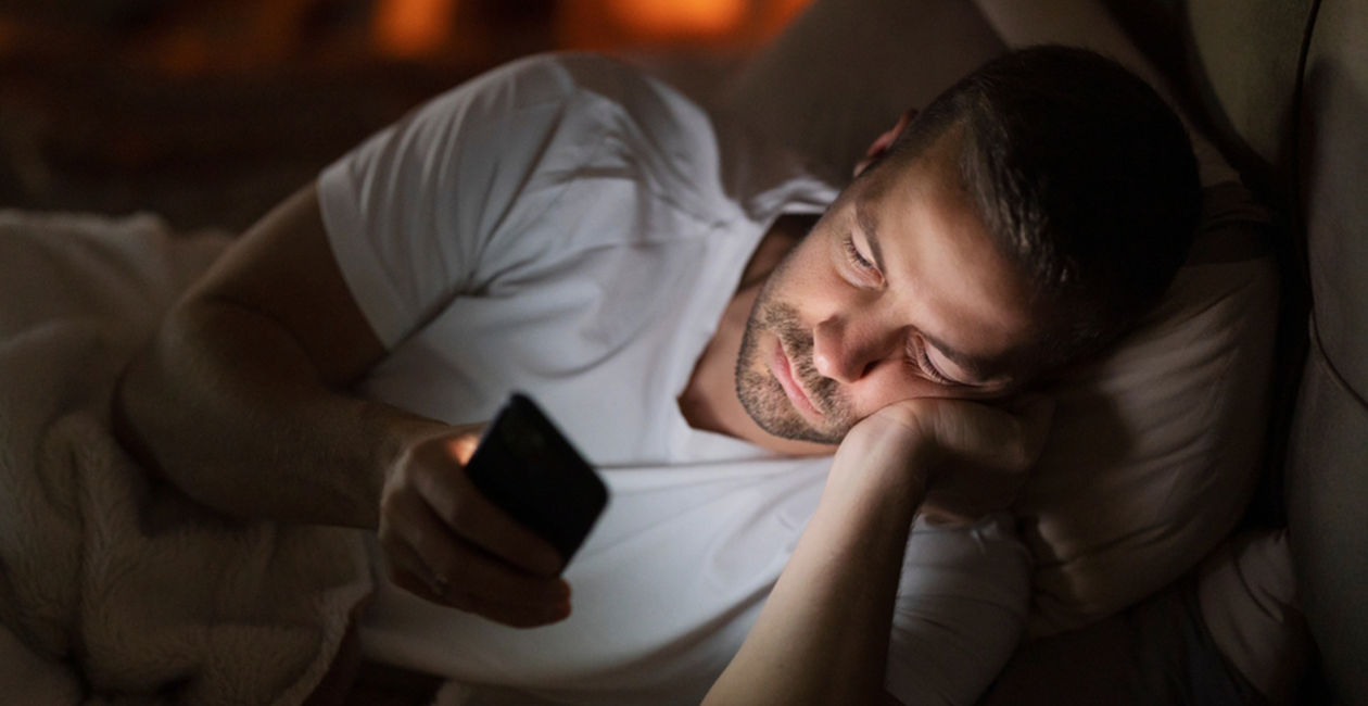 A man lying on his side in bed looking at the screen of his phone
