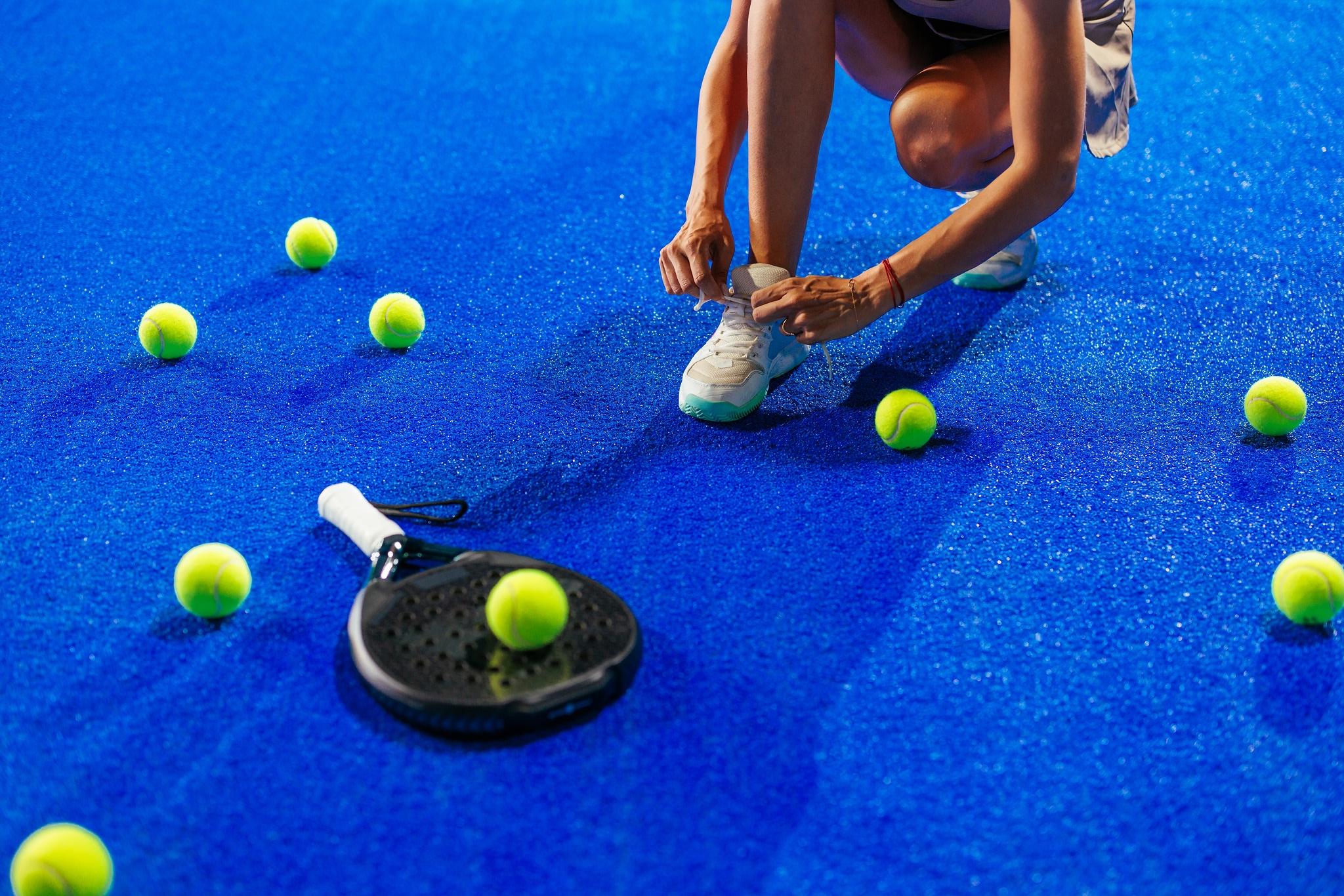 someone tying their shoe with a padel racket and multiple balls around them