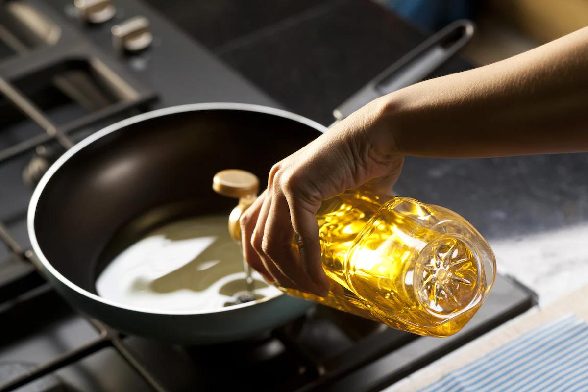 Someone pouring cooking oil into a wok on a gas hob