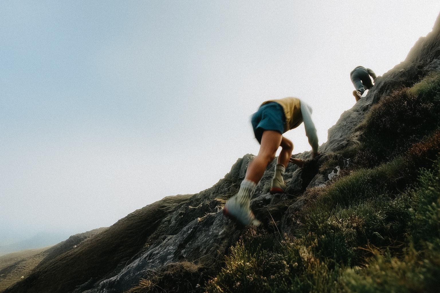 2 people clambering up some rocks in a mountainous area