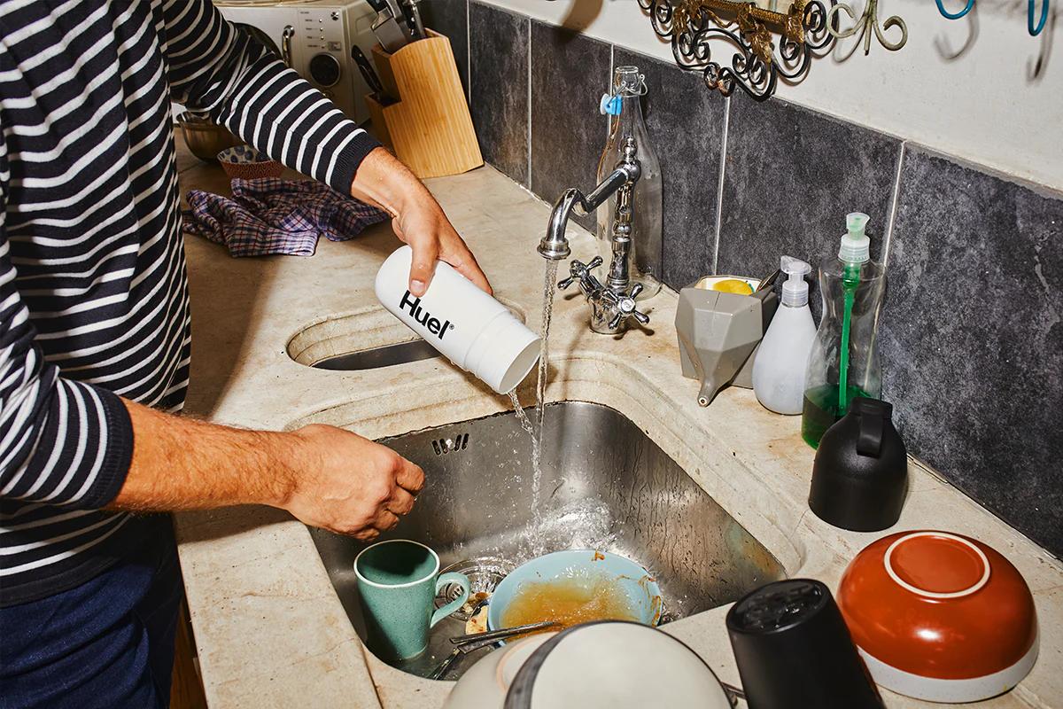 man cleaning their huel shaker in the sink which has dirty dishes in
